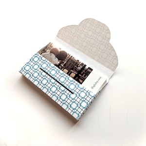 May include: A white and blue patterned box with a photo of two people inside. The box has a flap that opens to reveal the photo. The text "digibaby.com" is printed on the box.