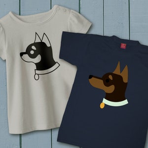 May include: Two t-shirts with a dog graphic design. The left shirt is light gray with a black dog graphic. The right shirt is navy blue with a brown dog graphic.