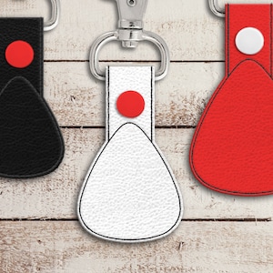 May include: Three leather keychains with a teardrop shape. The keychains are black, white, and red with a red circle on the black and white keychains and a white circle on the red keychain.