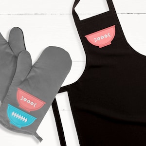 May include: A set of gray oven mitts with a pink and blue bowl design. The mitts are on a white wooden surface. The mitts are a great way to protect your hands from heat while cooking.