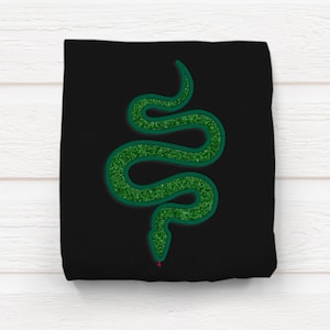 May include: Black square textile with a green glitter snake design. The snake is in a curved pose with a red dot at the tip of its head. The snake design is centered on the textile.