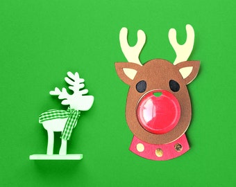 Peut inclure: Deux décorations de rennes en bois blanc sur un fond vert. Un renne porte une écharpe à carreaux verts et blancs et l'autre a un nez rouge.