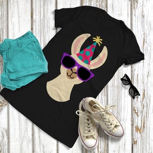 May include: Black t-shirt with a cartoon llama wearing sunglasses and a party hat. The llama has a pink and blue polka dot hat with a yellow sparkler on top. The sunglasses are purple.