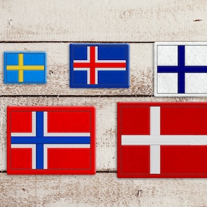 Könnte beinhalten: Fünf gestickte Stoff-Patches mit den Flaggen von Schweden, Island, Finnland, Norwegen und Dänemark. Die Patches sind in einer Reihe auf einem hellen Holzhintergrund angeordnet.