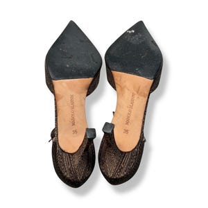 May include: A pair of Manolo Blahnik size 35 heels. The shoes have a pointed toe and a patterned fabric. The soles are black, and the heels have a small, square detail. The shoes are brown and black.
