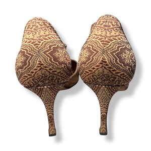 May include: A pair of high-heeled shoes with a brown and tan patterned design. The slender heels and the upper part of the shoes share the same detailed pattern. The shoes are displayed against a white backdrop.