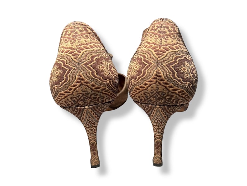 May include: A pair of high-heeled shoes with a brown and tan patterned design. The slender heels and the upper part of the shoes share the same detailed pattern. The shoes are displayed against a white backdrop.