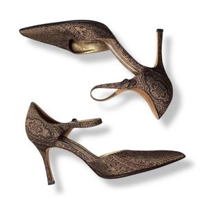 May include: A pair of brown high-heeled shoes with a pointed toe and ankle strap. The shoes have a paisley pattern in brown and gold. The heels are slender and the interior is gold.