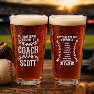 May include: Two pint glasses filled with beer, featuring baseball-themed designs. One glass says "Coach Scott" and the other lists names and the year 2026. A baseball, glove, and bat are also visible.