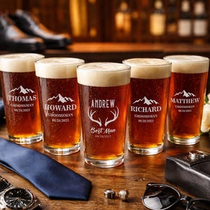 May include: Six pint glasses filled with beer, each with a personalized design. The glasses have names and titles like "Groomsman" and "Best Man" with a date. Accessories like a watch, tie, and sunglasses are on the wooden surface.
