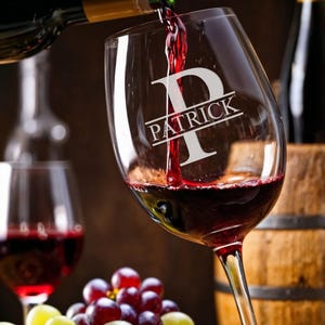 May include: A wine glass with the name "PATRICK" and a large "P" etched into the glass. Red wine is being poured into the glass from a bottle. Grapes are in a wooden bowl.