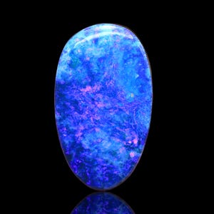May include: An oval-shaped cabochon gemstone featuring a vibrant play-of-color with deep blue, bright cyan, and flashes of magenta and purple throughout the surface. The stone has a smooth, polished finish and a rounded, dome-like top profile.