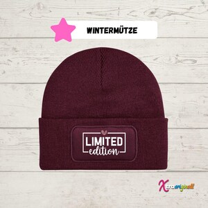 Könnte beinhalten: Eine bordeauxfarbene Mütze mit einem weißen Patch, auf dem "LIMITED edition" steht, mit einem kleinen rosa Herz über dem Wort "LIMITED".