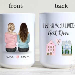 May include: White ceramic mug with a personalized design featuring two women with long hair, one with blonde hair and one with brown hair, sitting back to back. The mug has the names "Rosie" and "Emily" written on the front. The back of the mug has the text "I wish you lived next door" with two small houses and a heart.
