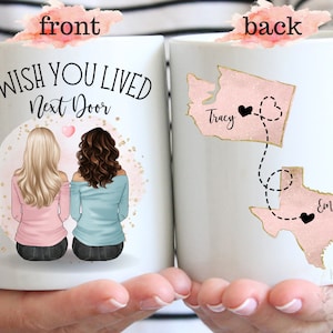 May include: White ceramic mug with a pink and gold design. The front of the mug features two women sitting back to back with the text "I wish you lived next door". The back of the mug features a map of the United States with two states highlighted in pink and gold with the text "Tracy" and "Emily" on each state.