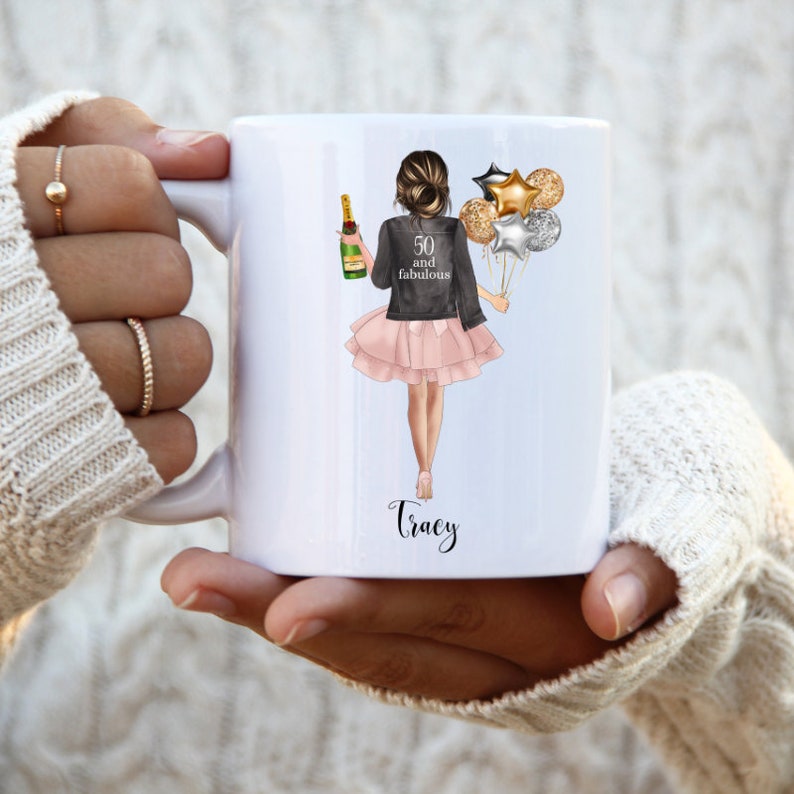 Peut inclure: Mug en c&eacute;ramique blanche avec un graphique d'une femme tenant une bouteille de champagne et des ballons. Le texte "50 and fabulous" est sur la veste de la femme. Le nom "Tracy" est &eacute;crit sous le graphique.