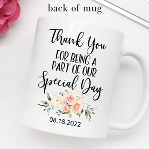 K&ouml;nnte beinhalten: Wei&szlig;e Keramiktasse mit einer schwarzen Aufschrift, die lautet "Vielen Dank, dass du Teil unseres besonderen Tages warst" mit einem Blumenmuster und dem Datum "08.18.2022".
