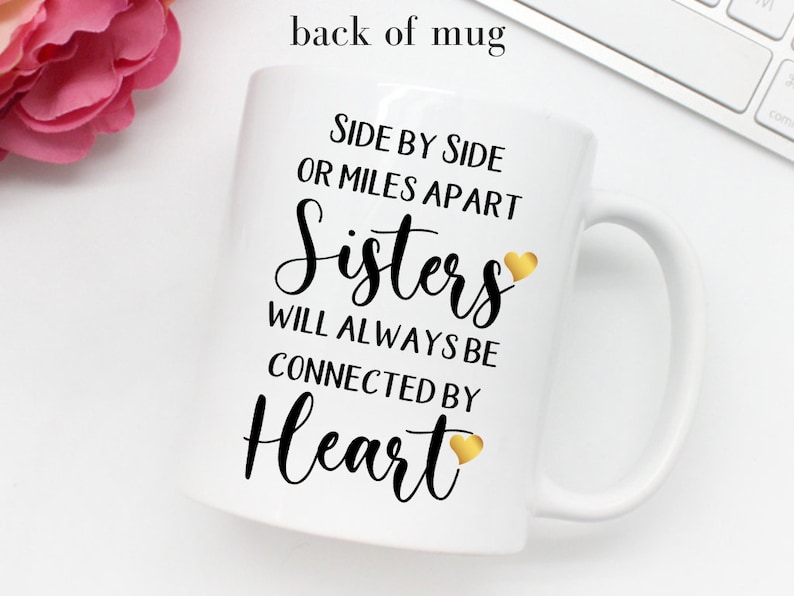 May include: White ceramic mug with black text that reads "Side by side or miles apart Sisters will always be connected by Heart" with a gold heart graphic after "Sisters" and "Heart".
