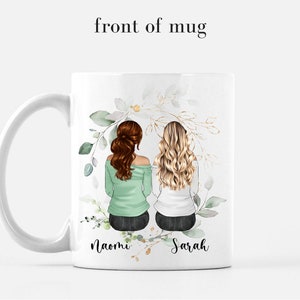 May include: White ceramic mug with a floral design featuring two women with brown and blonde hair sitting back to back. The mug has the names "Naomi" and "Sarah" written below the women.