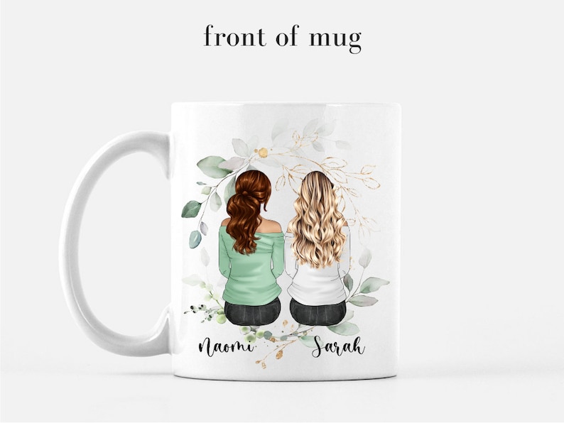 May include: White ceramic mug with a floral design featuring two women with brown and blonde hair sitting back to back. The mug has the names "Naomi" and "Sarah" written below the women.