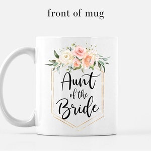 K&ouml;nnte beinhalten: Wei&szlig;e Keramiktasse mit goldenem geometrischem Rahmen und Blumendesign. Der Text "Aunt of the Bride" ist in Schwarz innerhalb des Rahmens geschrieben.