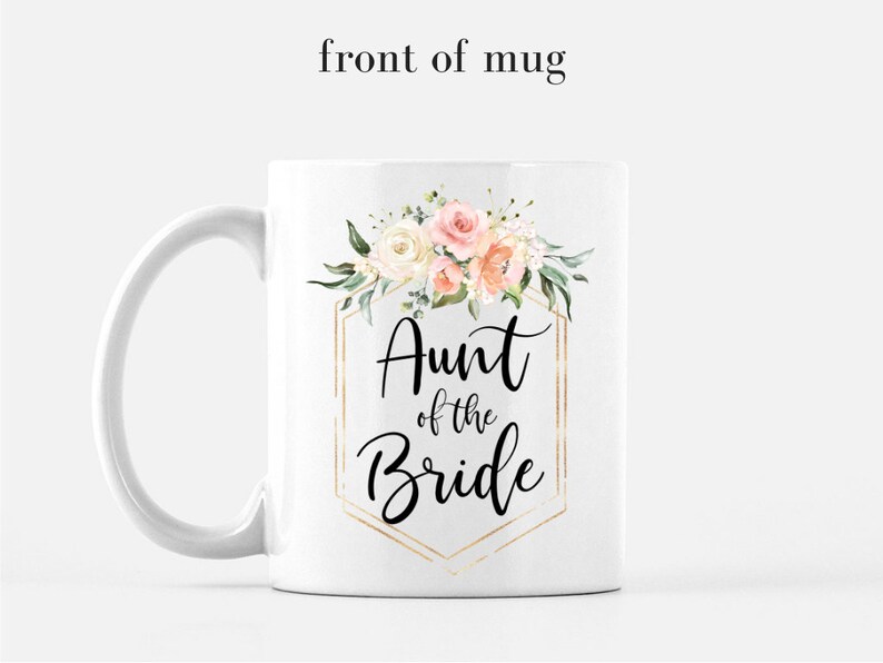 K&ouml;nnte beinhalten: Wei&szlig;e Keramiktasse mit goldenem geometrischem Rahmen und Blumendesign. Der Text "Aunt of the Bride" ist in Schwarz innerhalb des Rahmens geschrieben.