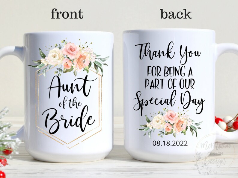 K&ouml;nnte beinhalten: Wei&szlig;e Keramiktasse mit einem goldenen geometrischen Rahmen und einem Blumendesign. Der Text "Aunt of the Bride" befindet sich im Rahmen. Die R&uuml;ckseite der Tasse hat den Text "Thank You for being a part of our Special Day" mit einem Blumendesign und dem Datum "08.18.2022".
