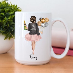 Peut inclure: Mug en c&eacute;ramique blanche avec un graphique d'une femme tenant une bouteille de champagne et des ballons. Le texte "50 and fabulous" est sur la veste de la femme. Le nom "Tracy" est imprim&eacute; au bas de la tasse.
