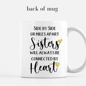 May include: White ceramic mug with a black and gold design. The mug features the text "Side by side or miles apart Sisters will always be connected by Heart" with a gold heart icon.