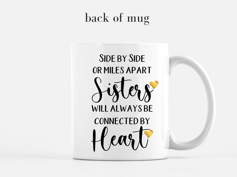 May include: White ceramic mug with a black and gold design. The mug features the text "Side by side or miles apart Sisters will always be connected by Heart" with a gold heart icon.