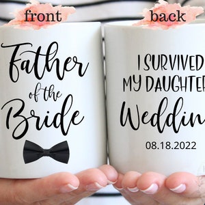 May include: White ceramic mug with black text and a black bow tie. The front of the mug reads "Father of the Bride". The back of the mug reads "I survived my daughter's wedding 08.18.2022".