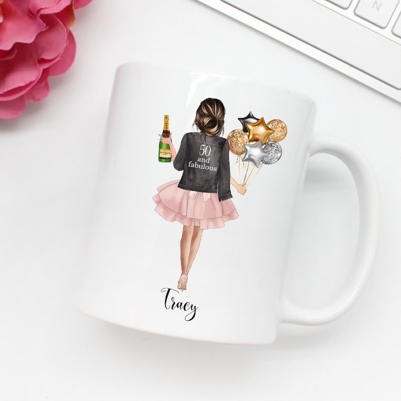 Peut inclure: Mug en c&eacute;ramique blanche avec un motif repr&eacute;sentant une femme tenant une bouteille de champagne et des ballons. Le texte "50 and fabulous" est sur la veste de la femme. Le nom "Tracy" est imprim&eacute; sur la tasse.
