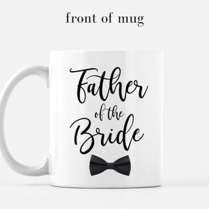 May include: White ceramic mug with a black inscription that reads "Father of the Bride" with a black bow tie underneath.
