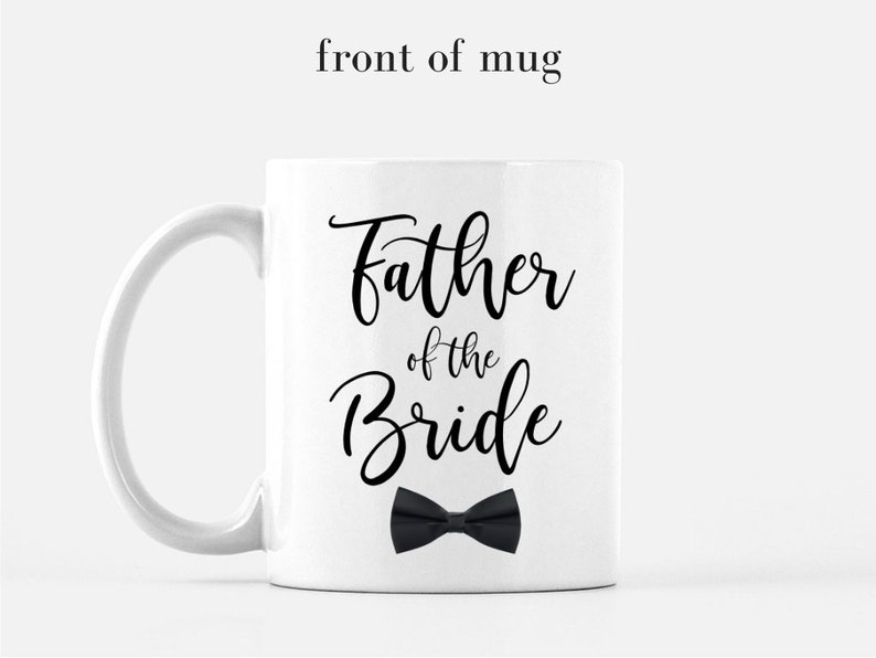 May include: White ceramic mug with a black inscription that reads "Father of the Bride" with a black bow tie underneath.