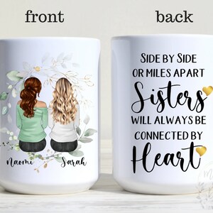 May include: White ceramic mug with a floral design and two women's illustrations on the front. The back of the mug has the text "Side by Side or Miles Apart Sisters Will Always Be Connected By Heart" with gold hearts.