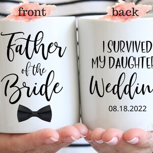 May include: White ceramic mug with black text and a black bow tie. The front of the mug reads "Father of the Bride". The back of the mug reads "I survived my daughter's wedding 08.18.2022".