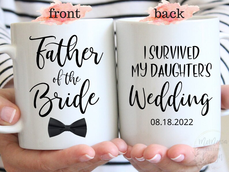 May include: White ceramic mug with black text and a black bow tie. The front of the mug reads "Father of the Bride". The back of the mug reads "I survived my daughter's wedding 08.18.2022".