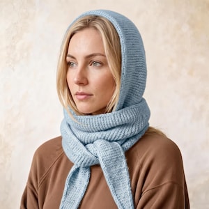May include: A light blue knitted balaclava hood with an integrated scarf design. The accessory features a textured ribbed knit pattern that covers the head and wraps around the neck, with two long ends hanging down in the front.