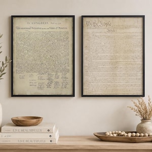 Könnte beinhalten: Zwei gerahmte Wandbilder mit historischen Dokumenten auf gealtertem, pergamentartigem Papier mit schwarzem Text. Der linke Druck zeigt die Unabhängigkeitserklärung, der rechte die Verfassung der Vereinigten Staaten mit dem Text We The People.
