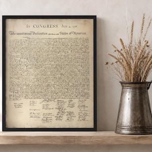 May include: Framed print of the Declaration of Independence, with the text "In Congress, July 4, 1776." The document is aged with a parchment-like appearance, set in a black frame. A metal pitcher with dried wheat stalks sits nearby.
