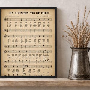 May include: A framed print featuring the musical score and lyrics for the song My Country 'Tis of Thee by Samuel Francis Smith, printed on aged parchment-colored paper with black text and musical notation, enclosed in a thin black frame.