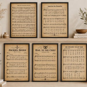 May include: A set of five framed wall art prints featuring vintage-style sheet music for The Star-Spangled Banner, America the Beautiful, Anchors Aweigh, Hail to the Chief, and My Country 'Tis of Thee, all displayed in black frames on a wooden shelf.