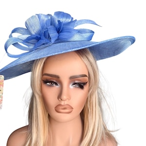 May include: A light blue, wide-brimmed hat with a large, decorative flower on top. The hat has a textured appearance and is likely made of a woven material. The flower is a lighter shade of blue and adds a touch of elegance to the design.