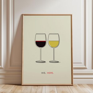 Op de afbeelding: Een ingelijste print met twee wijnglazen, één gevuld met rode wijn en de andere met witte wijn. De woorden "HIS. HERS." staan eronder gedrukt. De achtergrond is lichtbeige, de lijst is van hout.