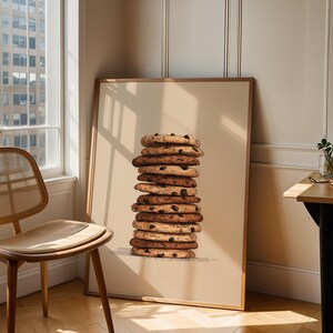 May include: A framed wall art print featuring a vertical stack of ten round chocolate chip cookies. The cookies are golden brown with visible dark chocolate chips, rendered in a detailed illustration style against a solid light beige background.