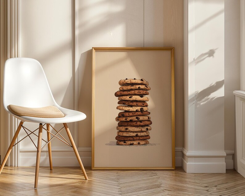 May include: A rectangular wall art print in a gold frame featuring a vertical stack of ten round chocolate chip cookies against a solid beige background. The cookies vary in shades of golden brown and dark brown, showing visible chocolate chips.