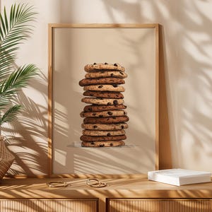 May include: A framed vertical wall art print featuring a tall, centered stack of round chocolate chip cookies. The illustration uses shades of brown and tan against a solid beige background, showcasing the textured edges of each cookie.