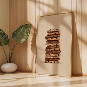 May include: A rectangular framed wall art print featuring a vertical stack of ten round chocolate chip cookies centered on a solid light beige background. The cookies are rendered in shades of golden brown with dark brown chocolate chips.