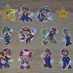 May include: A collection of holographic stickers featuring characters from the Super Mario video game series. The stickers include Mario, Luigi, Yoshi, Toad, Bowser, and star power-ups. The stickers are colorful and have a reflective, iridescent finish.