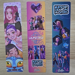 May include: Three colourful bookmarks featuring K-Pop Demon Hunters. The first bookmark has illustrations of three characters. The second bookmark has a heart and the word "HUNTRIX". The third bookmark has the text "K-POP DEMON HUNTERS".